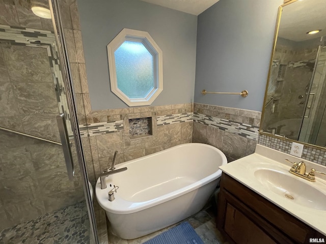 full bathroom featuring vanity, a stall shower, a soaking tub, wainscoting, and tile walls