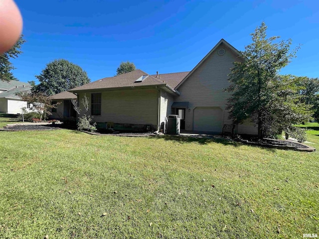 rear view of property featuring a garage, a yard, and central air condition unit