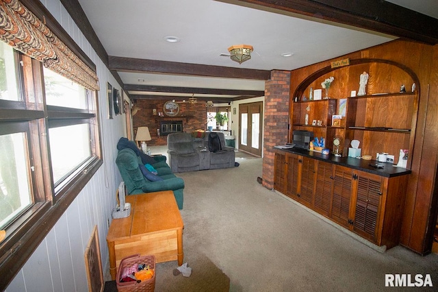 living room with a wealth of natural light, wooden walls, beamed ceiling, and a brick fireplace