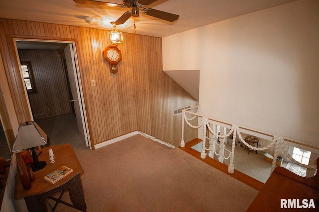 interior space featuring carpet, wooden walls, and ceiling fan