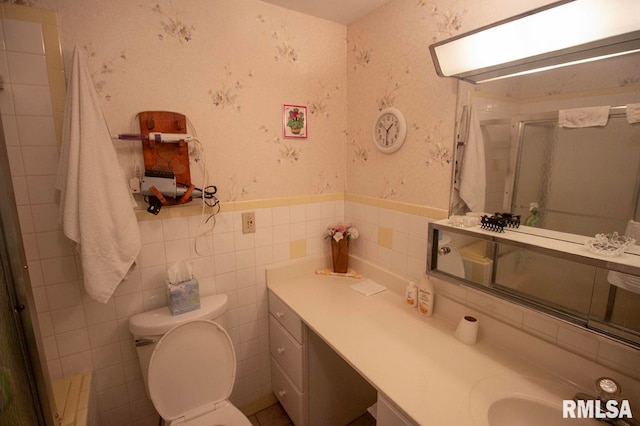 bathroom with tile walls, vanity, toilet, and a shower with door