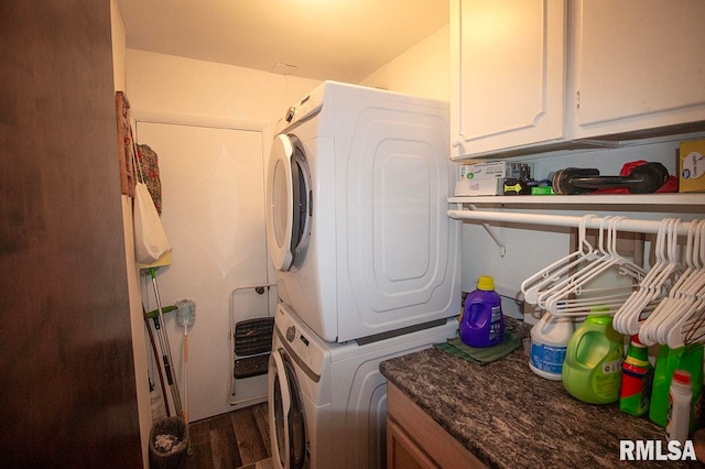 clothes washing area featuring cabinets, stacked washer and dryer, and dark wood-type flooring