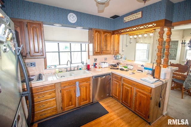 kitchen featuring light hardwood / wood-style floors, tile counters, sink, kitchen peninsula, and appliances with stainless steel finishes