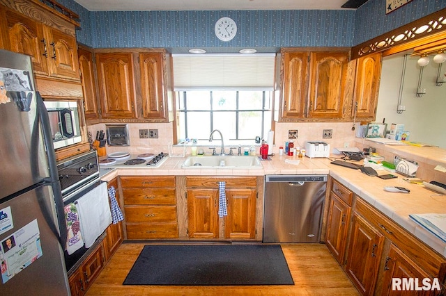 kitchen with light hardwood / wood-style floors, tasteful backsplash, stainless steel appliances, tile countertops, and sink