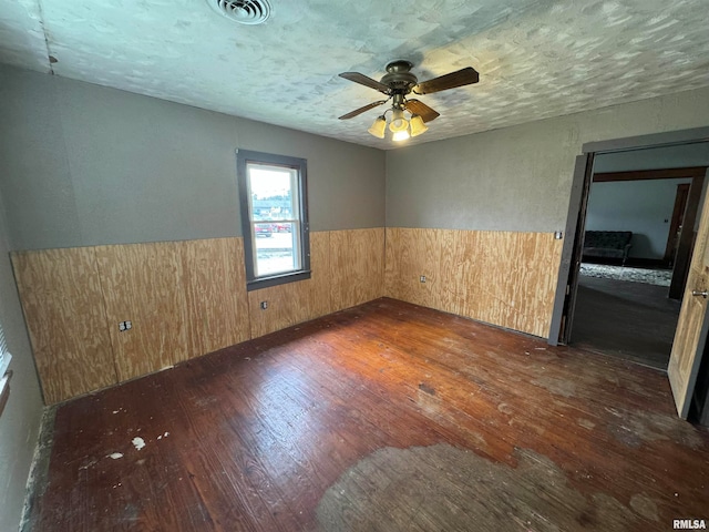 spare room with wooden walls, ceiling fan, a textured ceiling, and dark hardwood / wood-style flooring