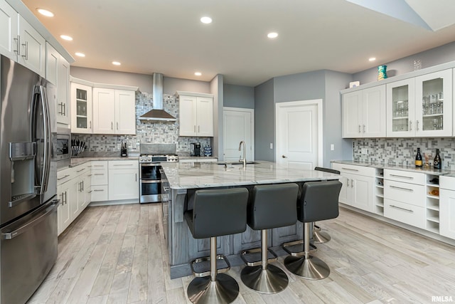 kitchen featuring white cabinetry, a center island with sink, wall chimney exhaust hood, and appliances with stainless steel finishes