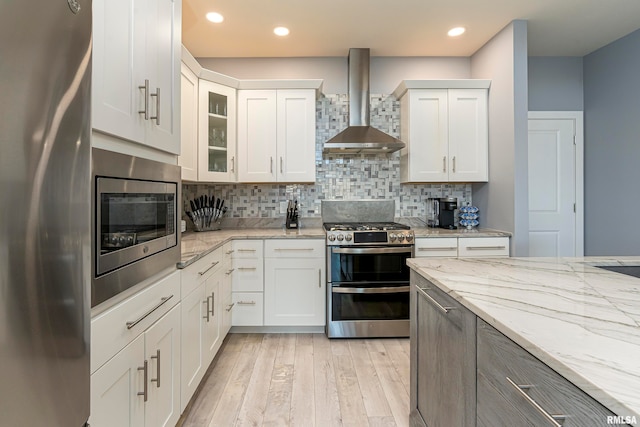 kitchen with white cabinets, wall chimney exhaust hood, decorative backsplash, light stone countertops, and stainless steel appliances