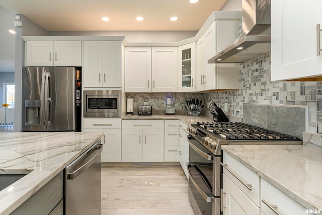 kitchen with white cabinetry, light stone countertops, wall chimney exhaust hood, backsplash, and appliances with stainless steel finishes