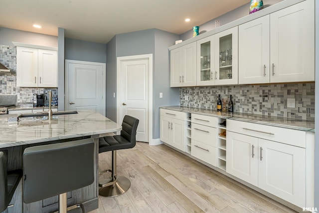 kitchen featuring a kitchen breakfast bar, sink, light stone countertops, tasteful backsplash, and white cabinetry