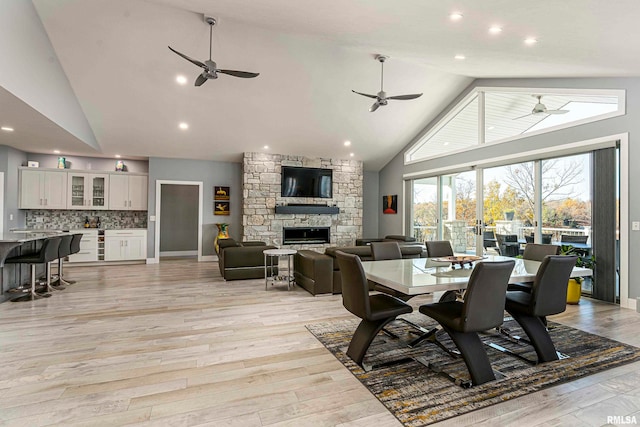 dining space featuring light wood-type flooring, a fireplace, and high vaulted ceiling