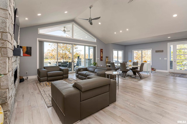 living room with ceiling fan, a fireplace, vaulted ceiling, and light wood-type flooring