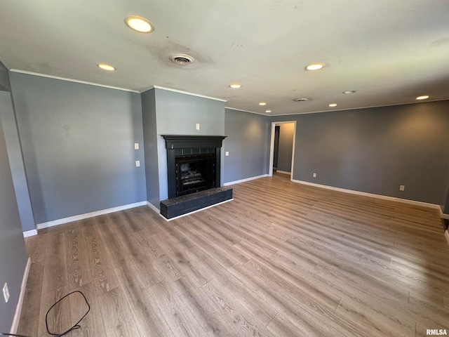 unfurnished living room featuring ornamental molding, a tiled fireplace, and light hardwood / wood-style floors