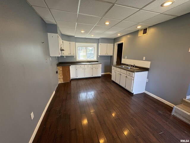 kitchen featuring a sink, baseboards, dark countertops, white cabinets, and a paneled ceiling