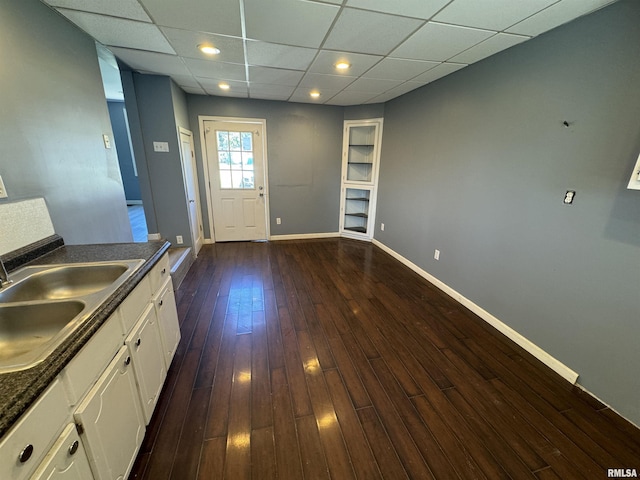 kitchen with a sink, white cabinets, dark countertops, baseboards, and dark wood-style flooring