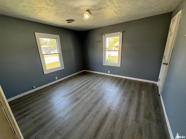 spare room featuring a textured ceiling, dark wood-style floors, and baseboards