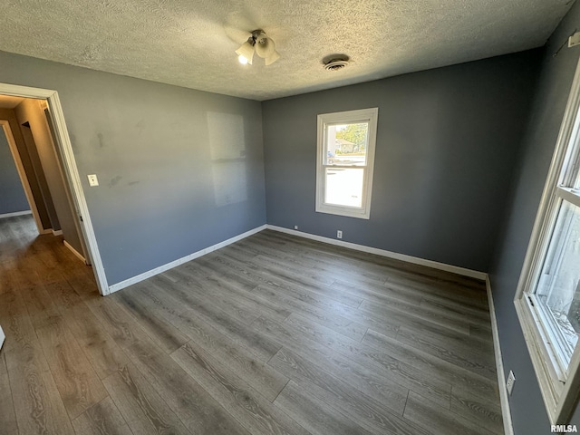 unfurnished room with a textured ceiling, dark wood-style floors, and baseboards