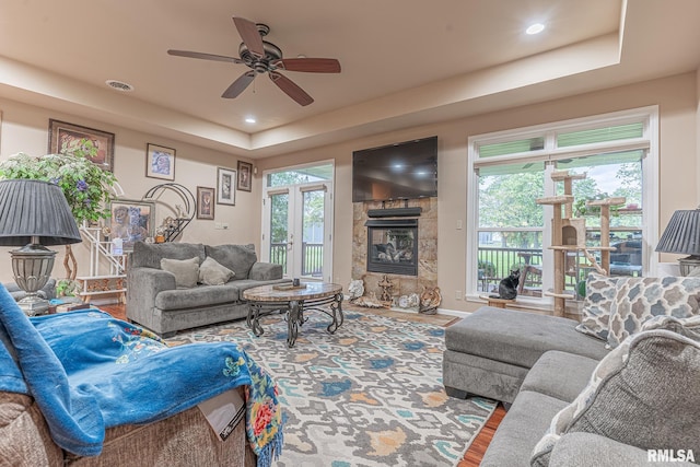 living room featuring a tiled fireplace, ceiling fan, plenty of natural light, and hardwood / wood-style floors