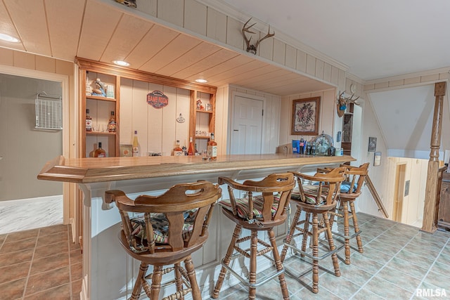 bar with crown molding, wooden walls, and tile patterned flooring