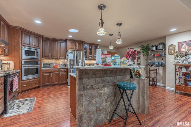 kitchen featuring wood-type flooring, a kitchen bar, stainless steel appliances, decorative light fixtures, and a center island