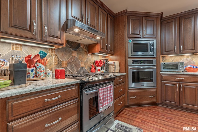 kitchen with light stone countertops, stainless steel appliances, light wood-type flooring, and tasteful backsplash