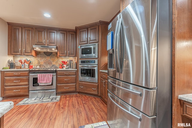 kitchen with light stone countertops, hardwood / wood-style floors, decorative backsplash, and stainless steel appliances