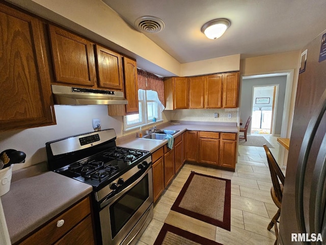 kitchen featuring light tile patterned floors, stainless steel gas range oven, sink, and washing machine and dryer