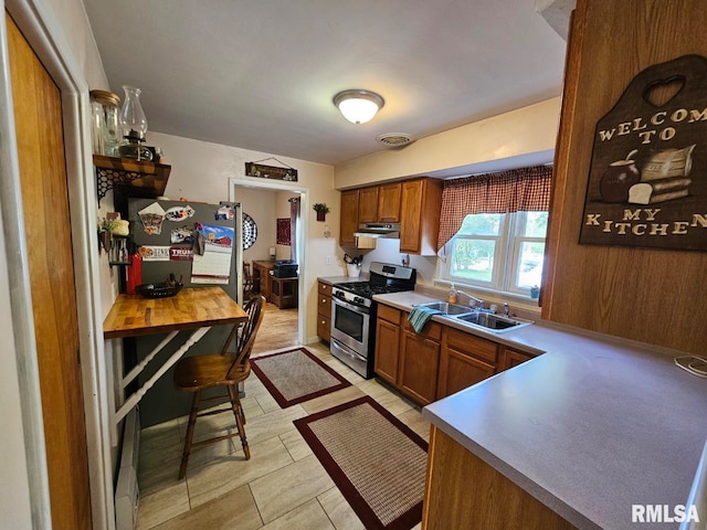 kitchen featuring a kitchen breakfast bar, wood walls, stainless steel range with gas stovetop, refrigerator, and sink