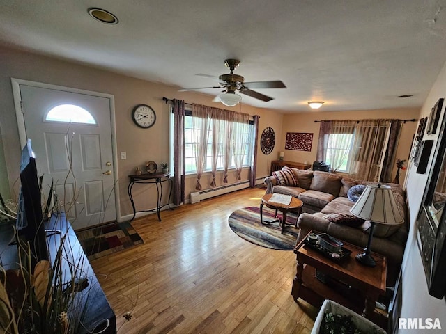 living room featuring light wood-type flooring, ceiling fan, baseboard heating, and plenty of natural light