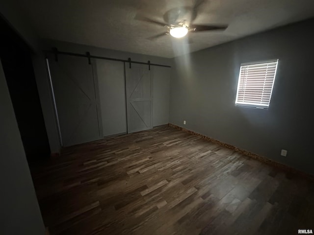 unfurnished bedroom with dark hardwood / wood-style flooring, ceiling fan, and a barn door