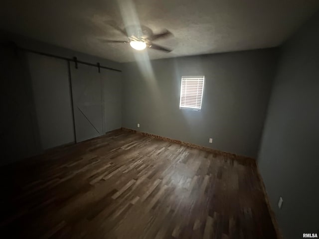 unfurnished bedroom with a barn door, dark hardwood / wood-style floors, ceiling fan, and a closet