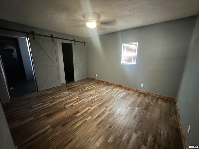 unfurnished bedroom with a barn door, a textured ceiling, dark hardwood / wood-style flooring, and ceiling fan