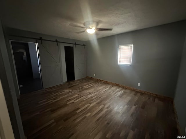 unfurnished bedroom featuring a closet, ceiling fan, dark hardwood / wood-style floors, and a barn door