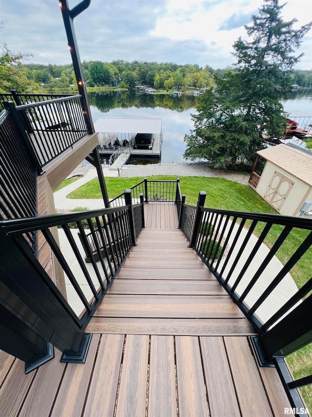 wooden deck with a storage unit, a water view, and a lawn