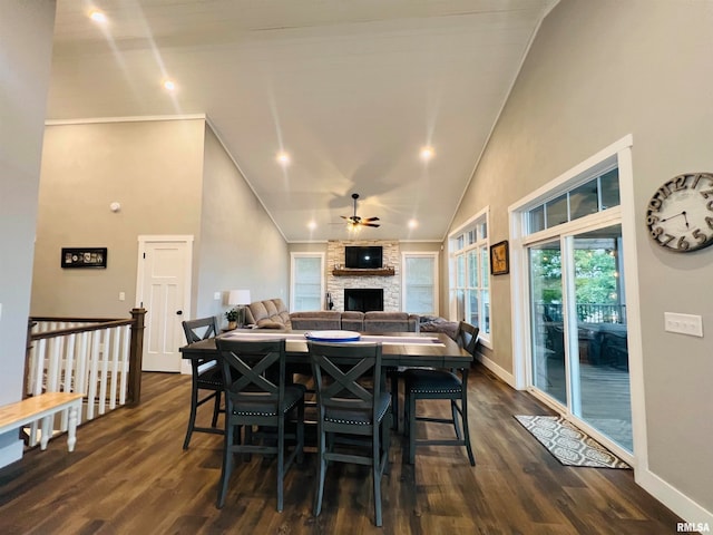 dining room with a stone fireplace, dark hardwood / wood-style floors, ceiling fan, and high vaulted ceiling