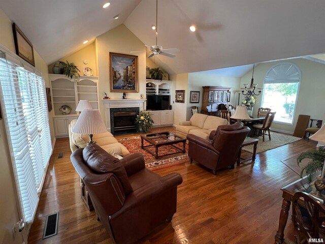 living room featuring ceiling fan with notable chandelier, wood-type flooring, a premium fireplace, and high vaulted ceiling