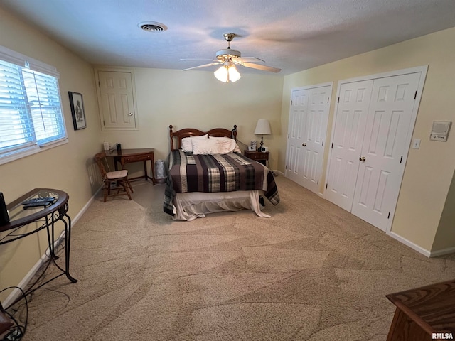 bedroom featuring ceiling fan, multiple closets, a textured ceiling, and carpet flooring