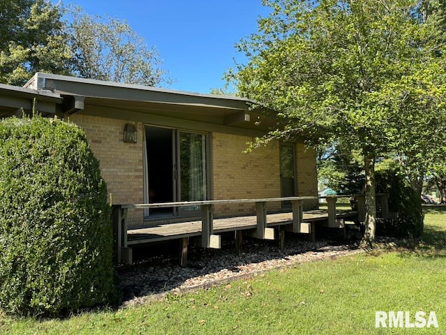 view of side of home with a deck, a lawn, and brick siding