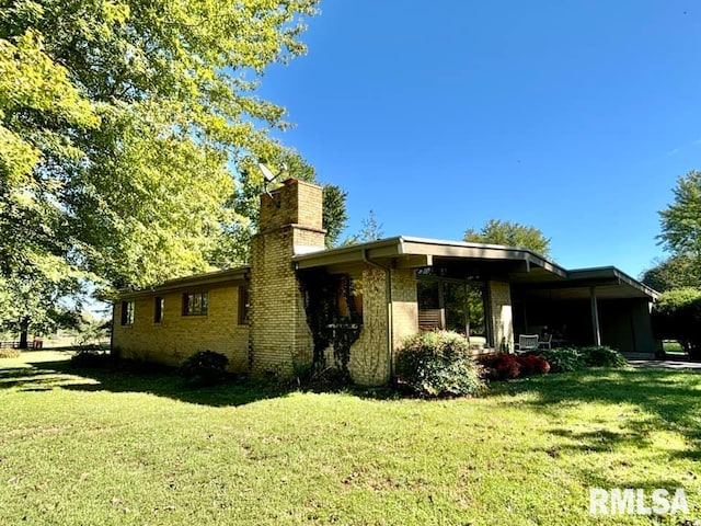 back of house with brick siding, a lawn, and a chimney