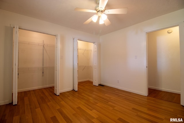 unfurnished bedroom with multiple closets, ceiling fan, and hardwood / wood-style flooring