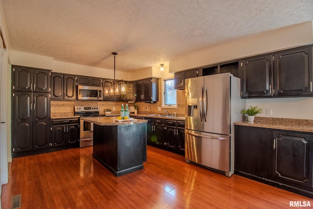 kitchen featuring hardwood / wood-style flooring, decorative light fixtures, a kitchen island, and stainless steel appliances