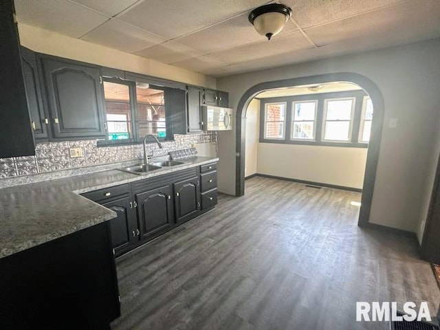 kitchen featuring decorative backsplash, dark wood-type flooring, a drop ceiling, stone counters, and sink