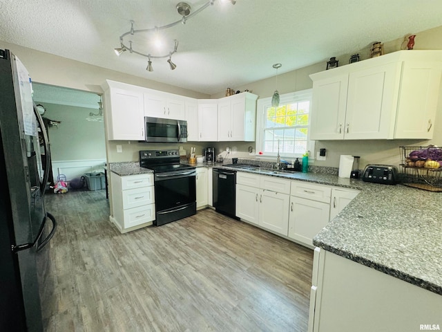 kitchen with light stone counters, black appliances, white cabinets, hanging light fixtures, and light hardwood / wood-style flooring