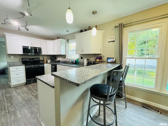 kitchen with pendant lighting, plenty of natural light, white cabinets, and black appliances