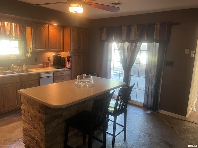kitchen with a center island, baseboards, a sink, light countertops, and ceiling fan