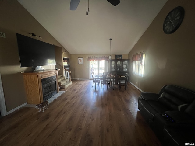 dining space featuring high vaulted ceiling, a ceiling fan, a glass covered fireplace, wood finished floors, and baseboards