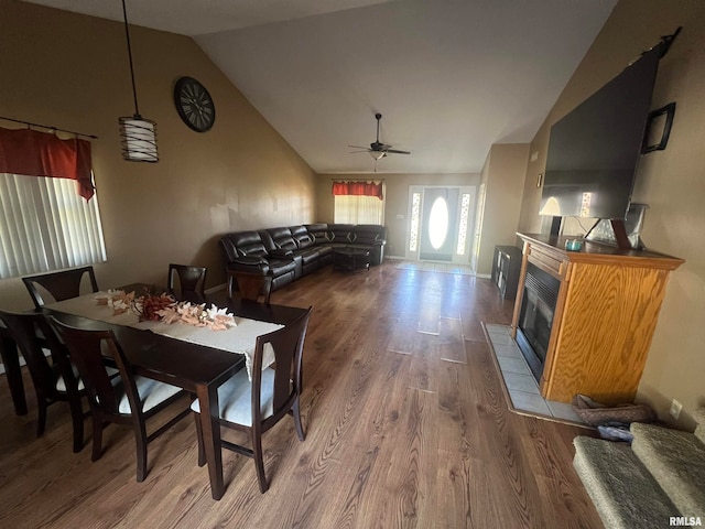 dining area with hardwood / wood-style floors, ceiling fan, a tiled fireplace, and vaulted ceiling