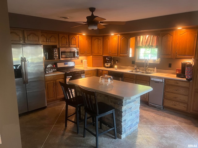 kitchen featuring ceiling fan, a center island, stainless steel appliances, sink, and a kitchen bar