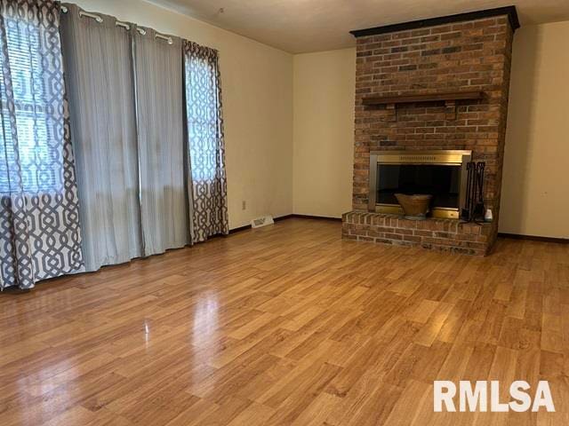 unfurnished living room with a brick fireplace, light hardwood / wood-style flooring, and a healthy amount of sunlight