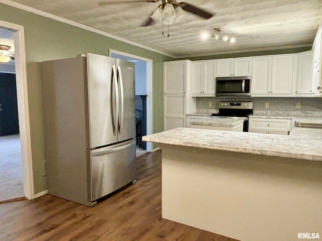 kitchen featuring dark wood-type flooring, stainless steel appliances, backsplash, ornamental molding, and white cabinetry