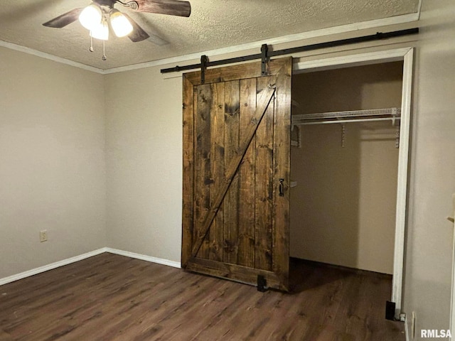 unfurnished bedroom featuring ceiling fan, a textured ceiling, a closet, a barn door, and dark hardwood / wood-style flooring